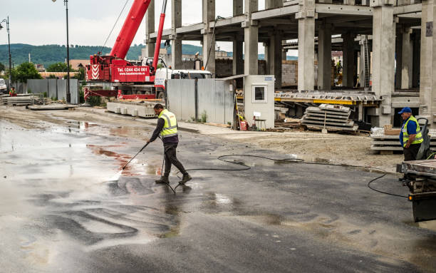 worker washing pavement with water post construction building site.