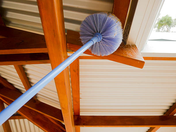 Cobweb brush sweeping under the roof in residential construction cleaning services.